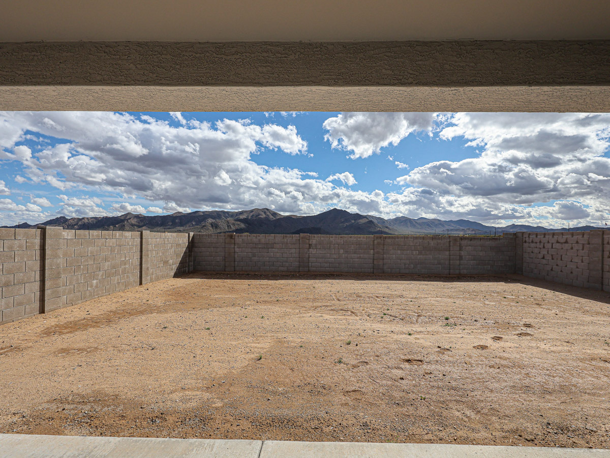 A large dirt field with a fence and mountains in the background.