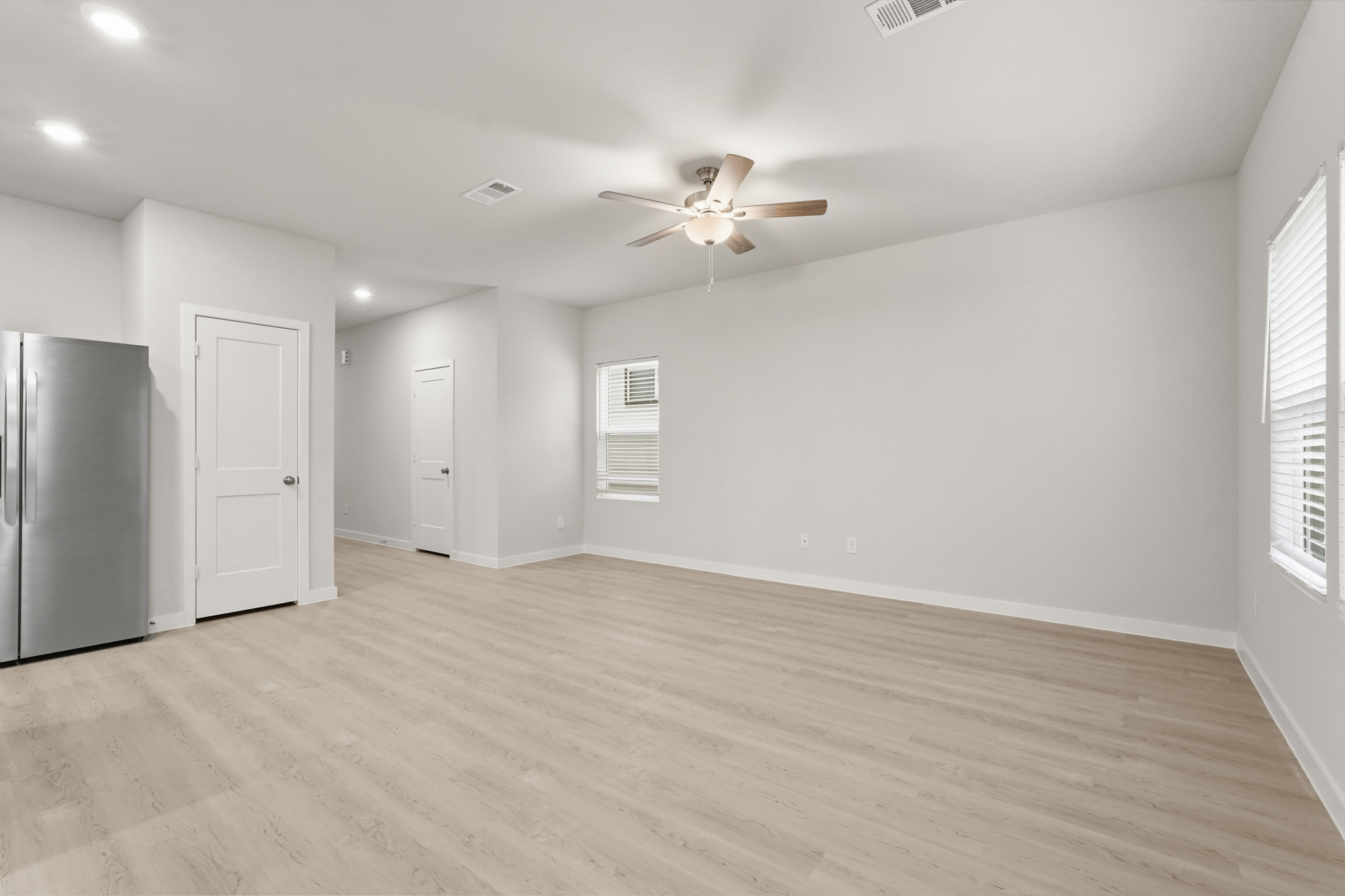 A large empty room with a ceiling fan and a wood floor.