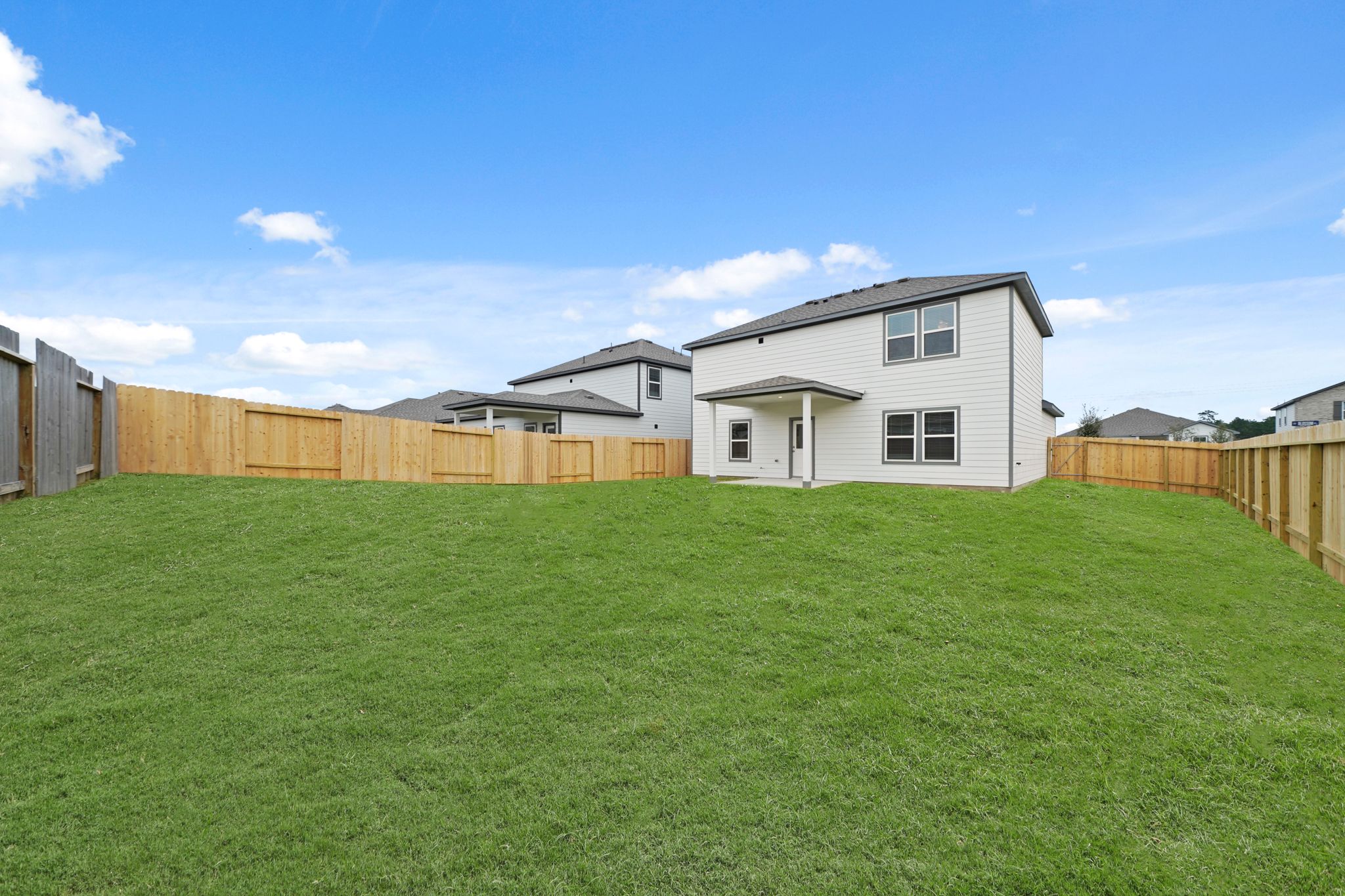 A green lawn with a fence and a house in the background.